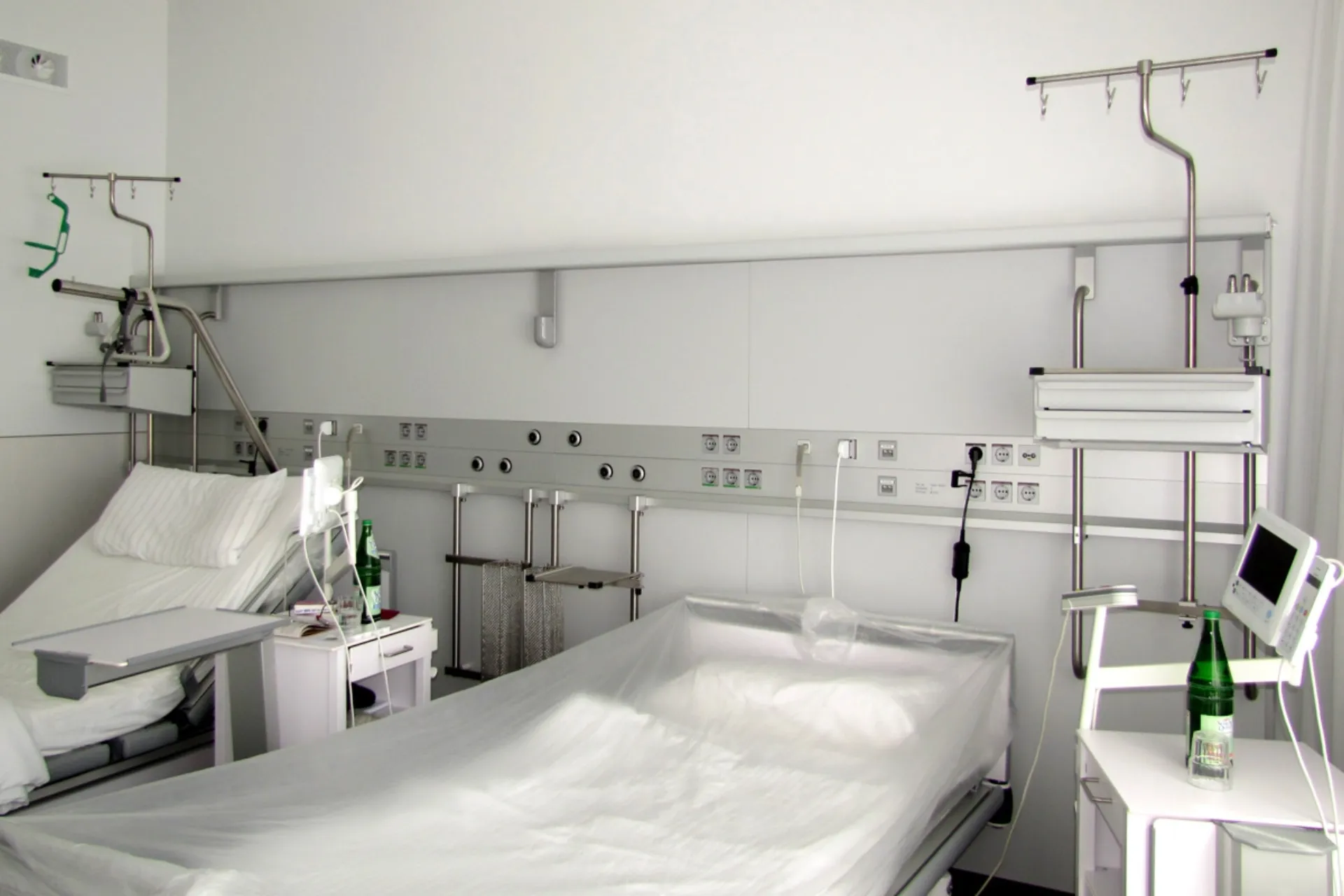 Zwei leere Krankenhausbetten mit medizinischen Geräten und Infusionsständern in einem hellen Patientenzimmer