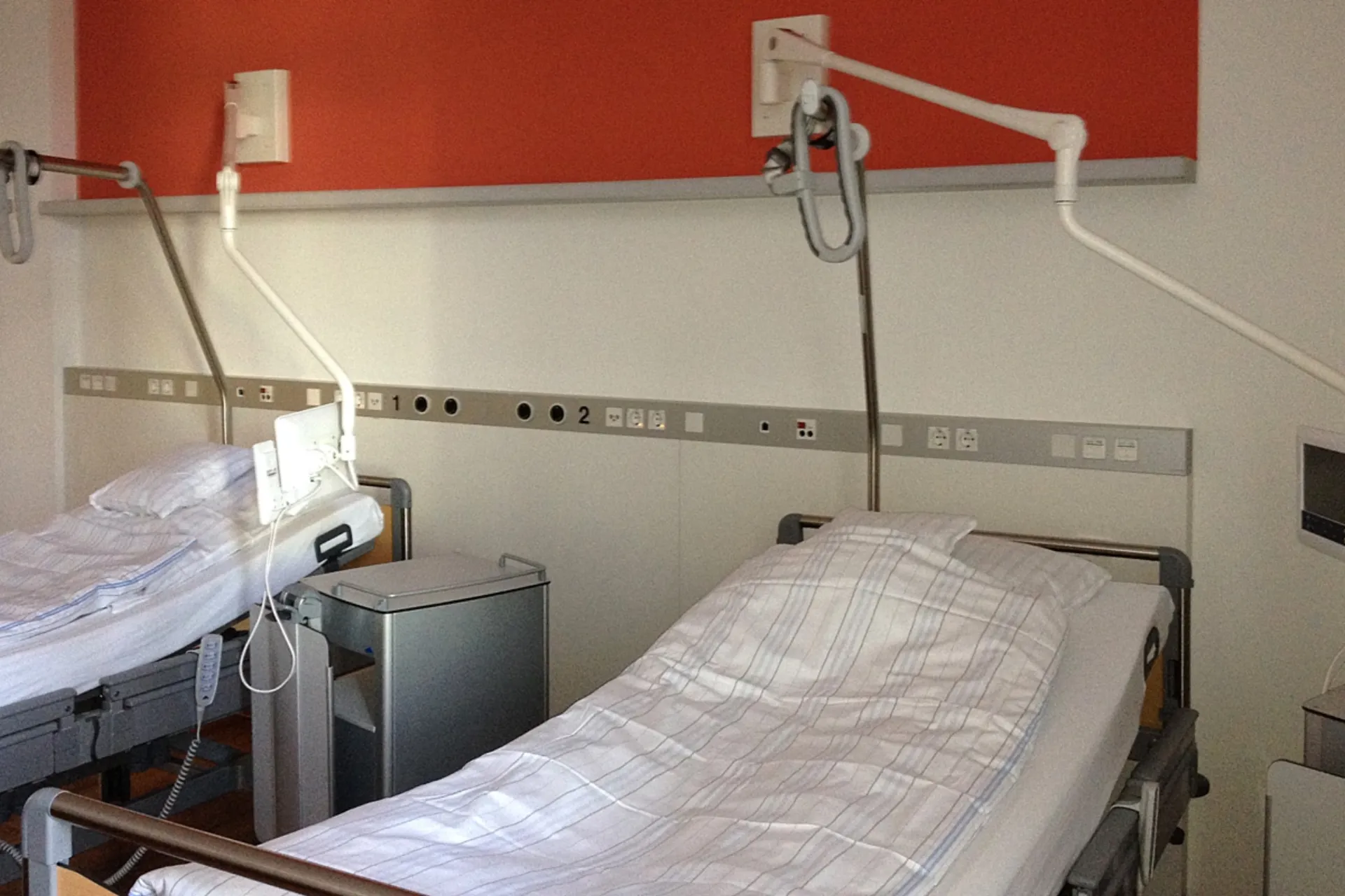 Zwei Krankenhausbetten mit weißen Bettlaken und verstellbaren Leselampen an der Wand in einem Patientenzimmer