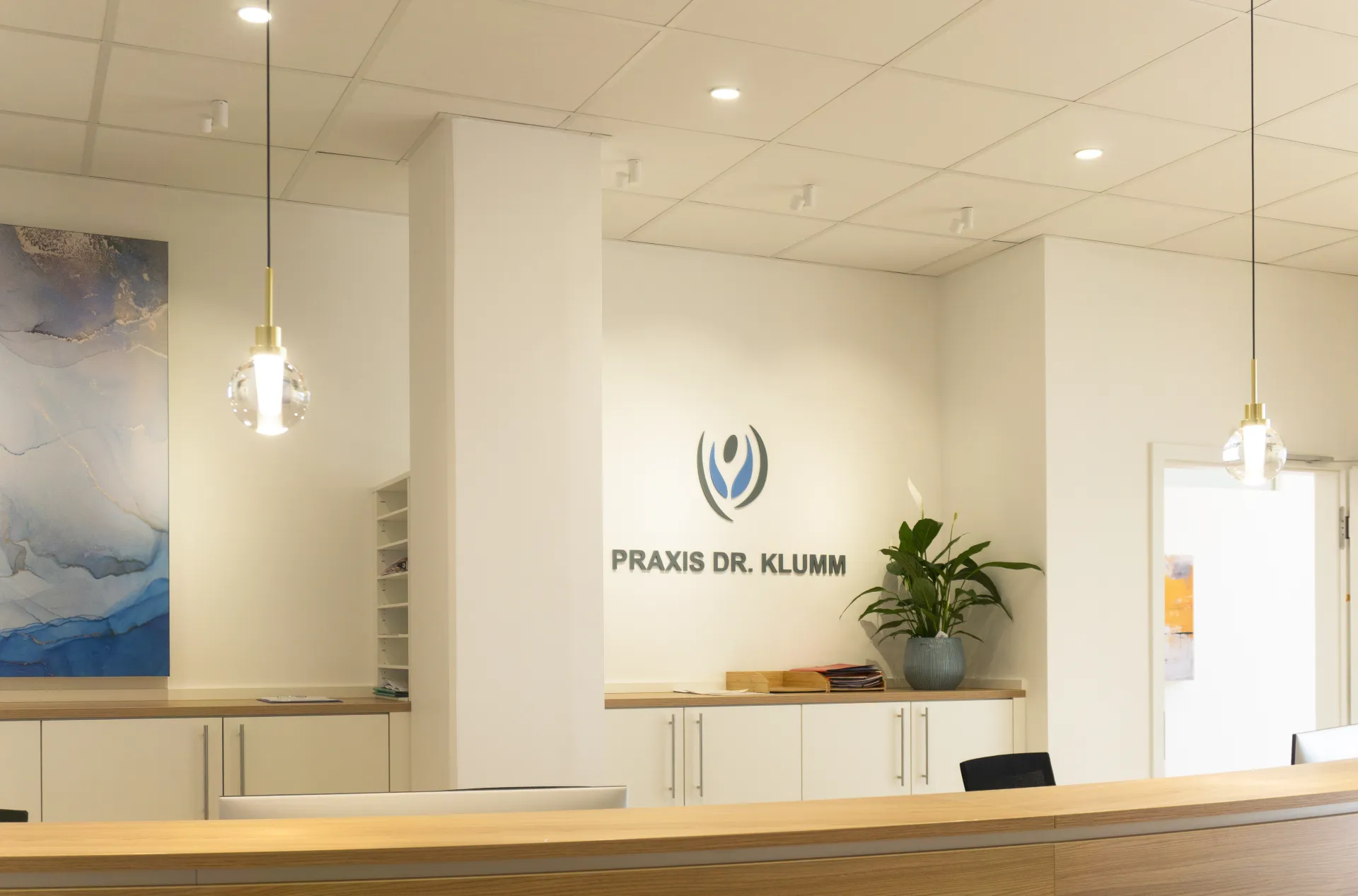 Eingangsbereich einer Praxis, beleuchtet mit Kugelpendelleuchte Alaska, Downlight Stram und Downlight Buddy.