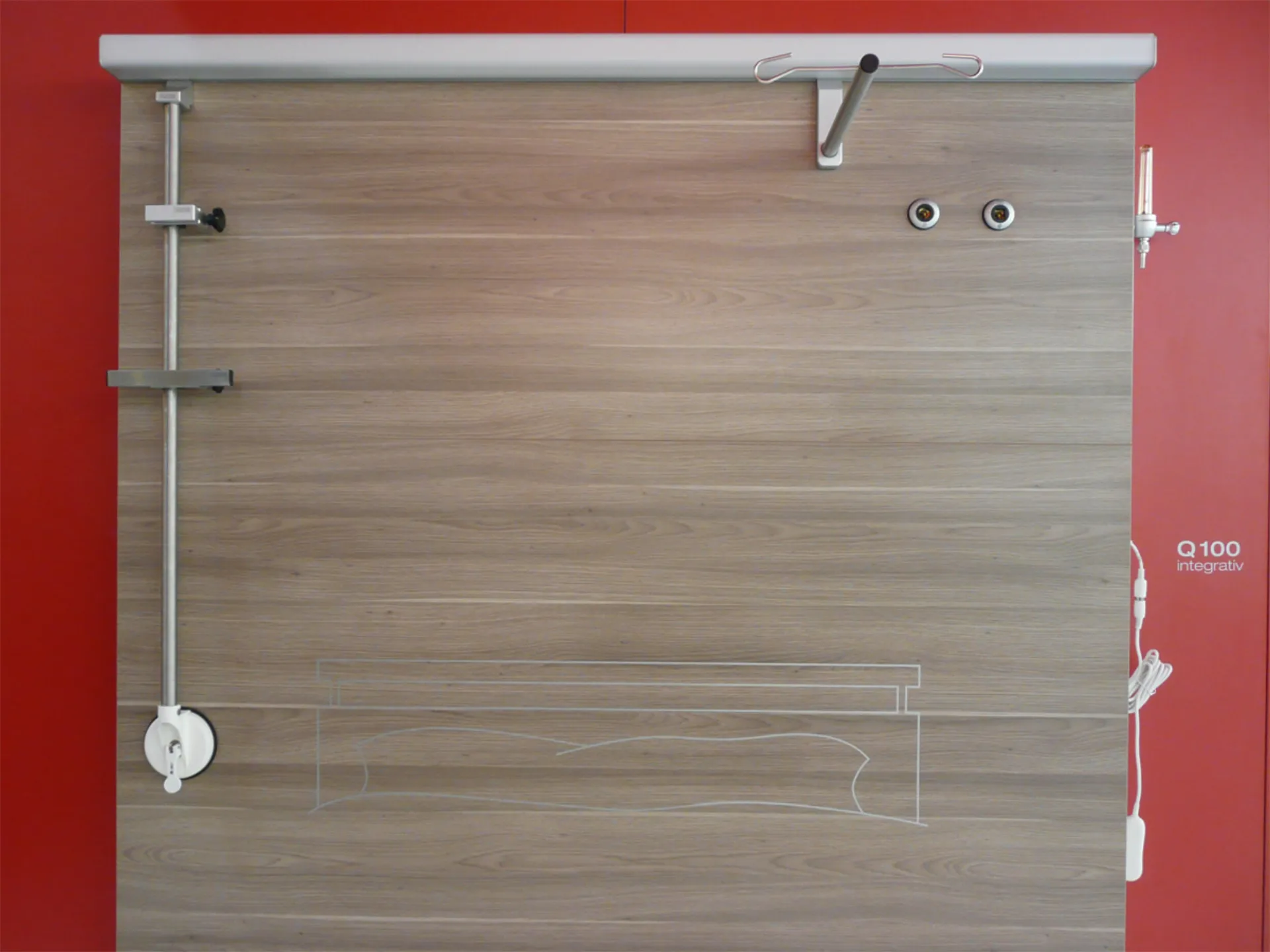 Holzplatte mit Metallstangen und -rollen an der linken und oberen Seite vor roter Wand mit weißem Schriftzug 'Q100 integrativ'