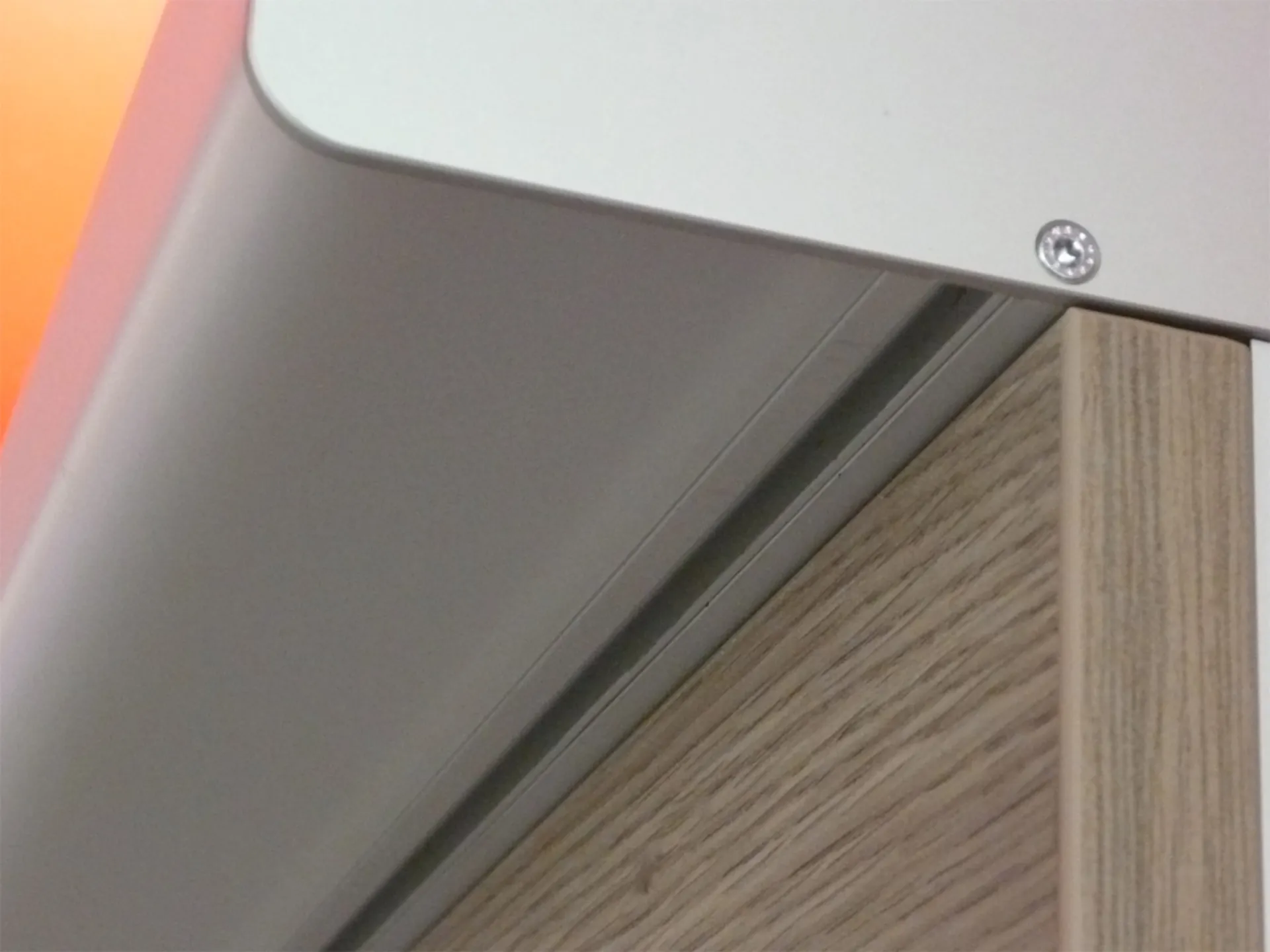 Nahaufnahme einer Holzplatte mit Metallprofil und Schraube in der Ecke