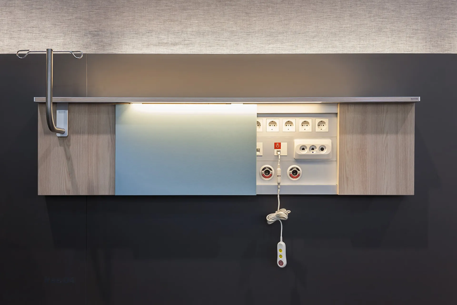 Wandmontierte Medizinische Versorgungseinheit mit Holzverkleidung, mehreren Steckdosen, medizinischen Gasanschlüssen, einem Infusionsständer und einem hängenden Bedienelement