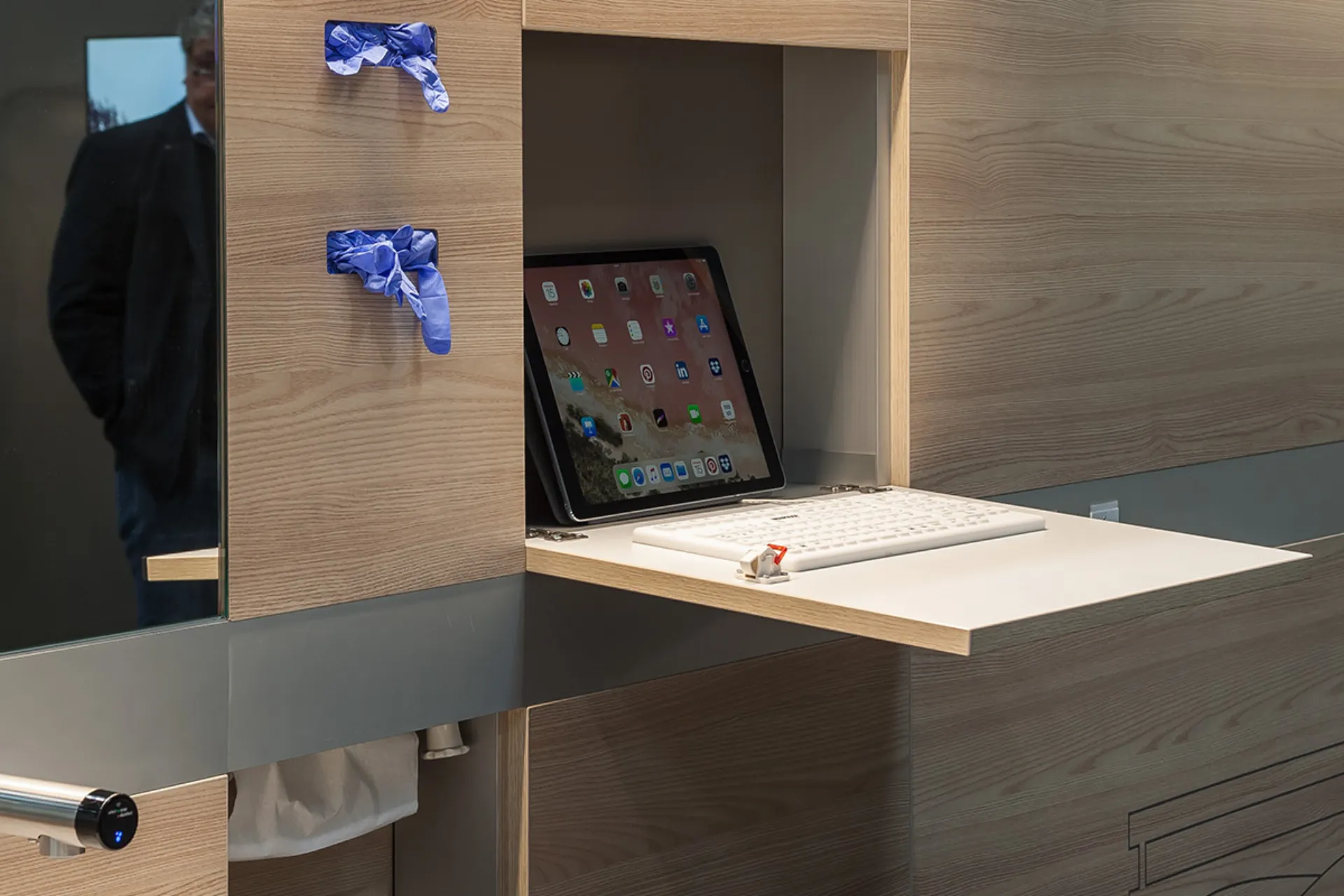 Tablet mit vielen App-Symbolen steht auf einem ausziehbaren Holztablett neben einer weißen Tastatur in einem modernen Holzregal